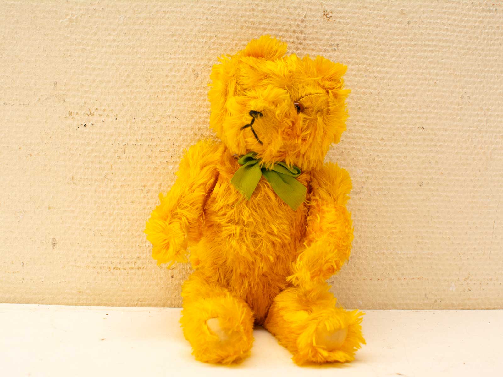 Charming vintage yellow teddy bear with green bow, exuding nostalgia and warmth. Perfect cuddle companion!