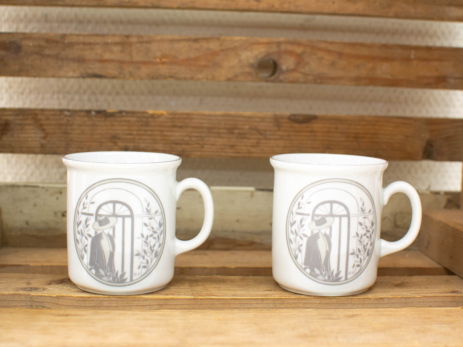 Elegant vintage porcelain mugs with gray illustration on rustic wood, perfect for stylish decor.