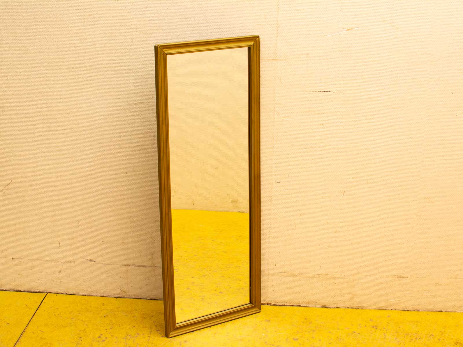 Elegant gold mirror against a beige wall with a vibrant yellow floor, perfect for any space.