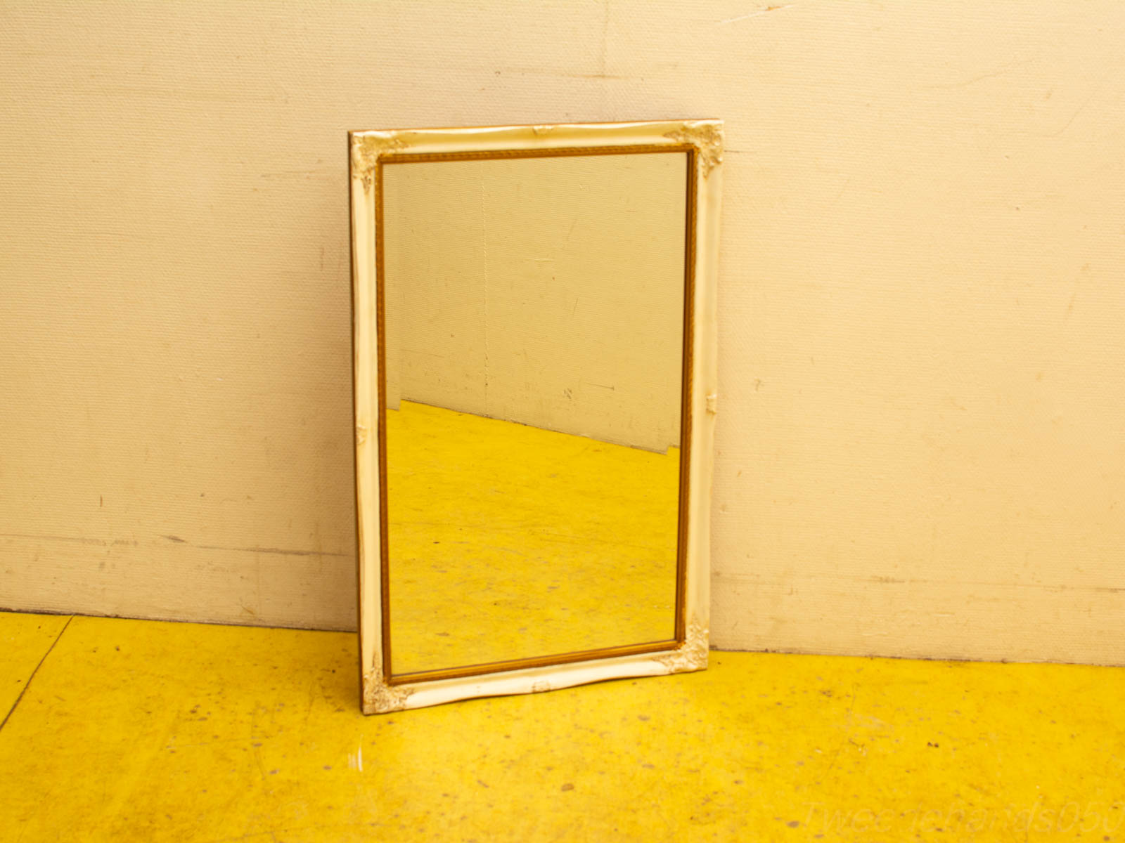 Vintage mirror with elegant white and gold frame against a cheerful yellow floor.