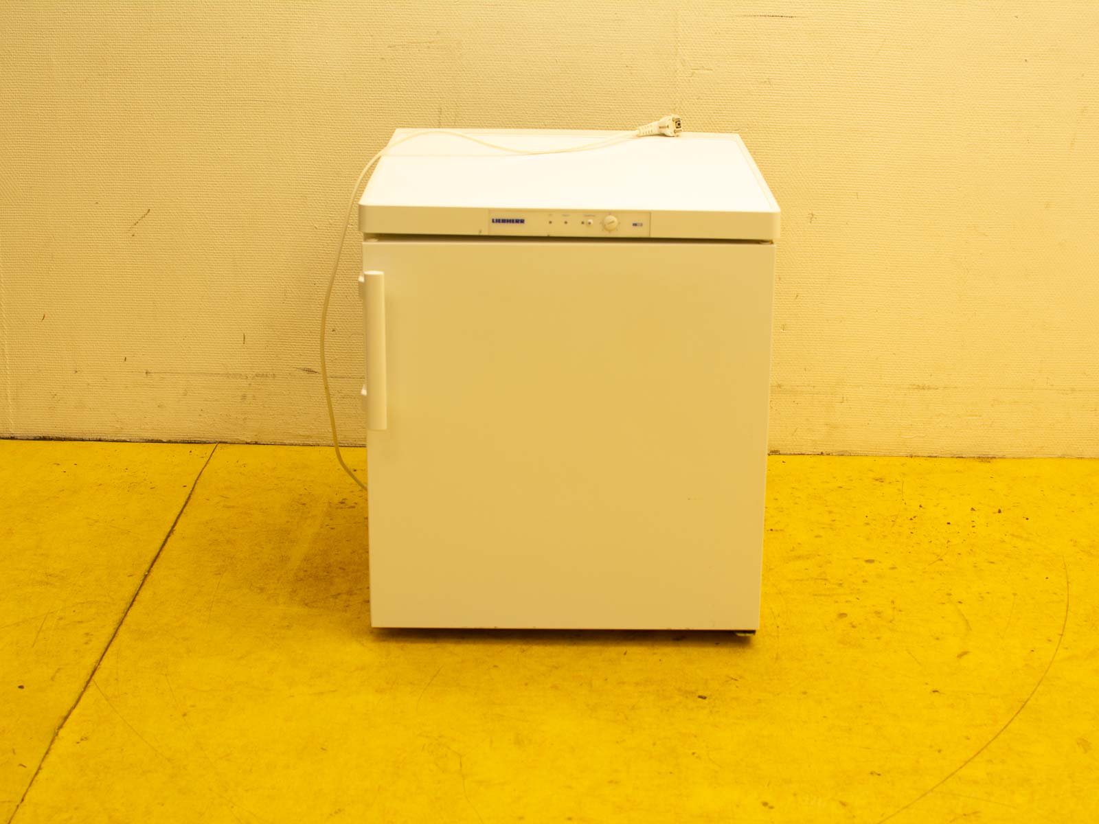 Compact white refrigerator against textured wall, perfect for stylish and functional kitchen spaces.