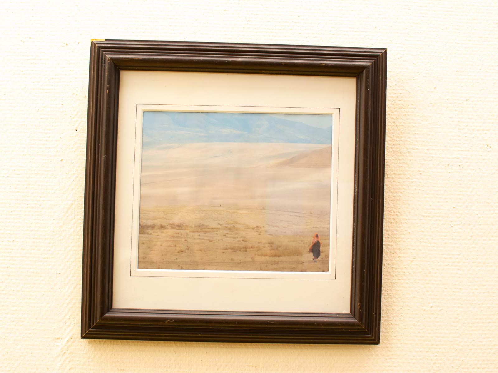 Solitary figure walking through serene desert dunes under a soft blue sky.