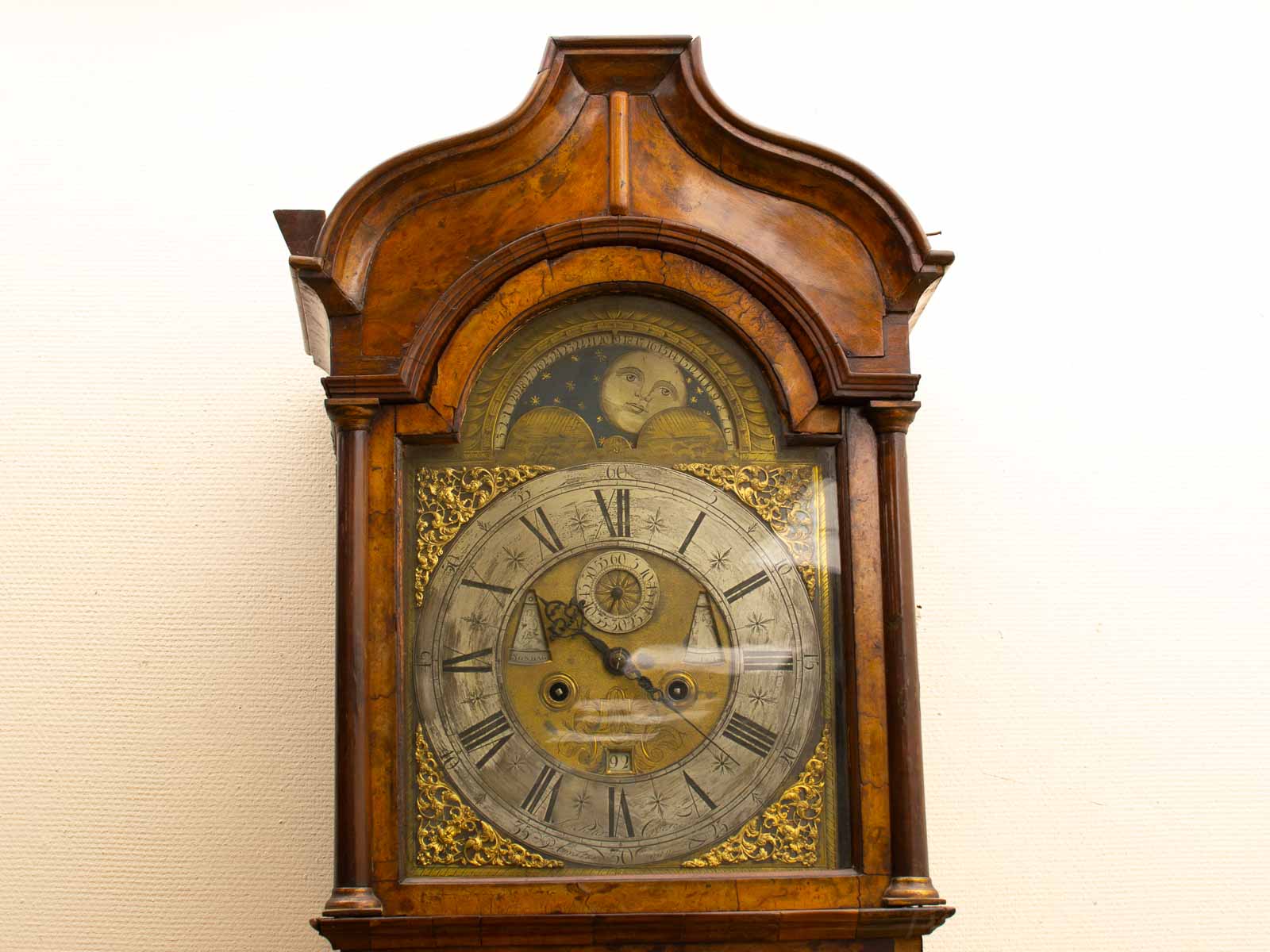 Close-up van de wijzerplaat van een Amsterdamse staand horloge klok met sierlijke gravures en antieke Romeinse cijfers.