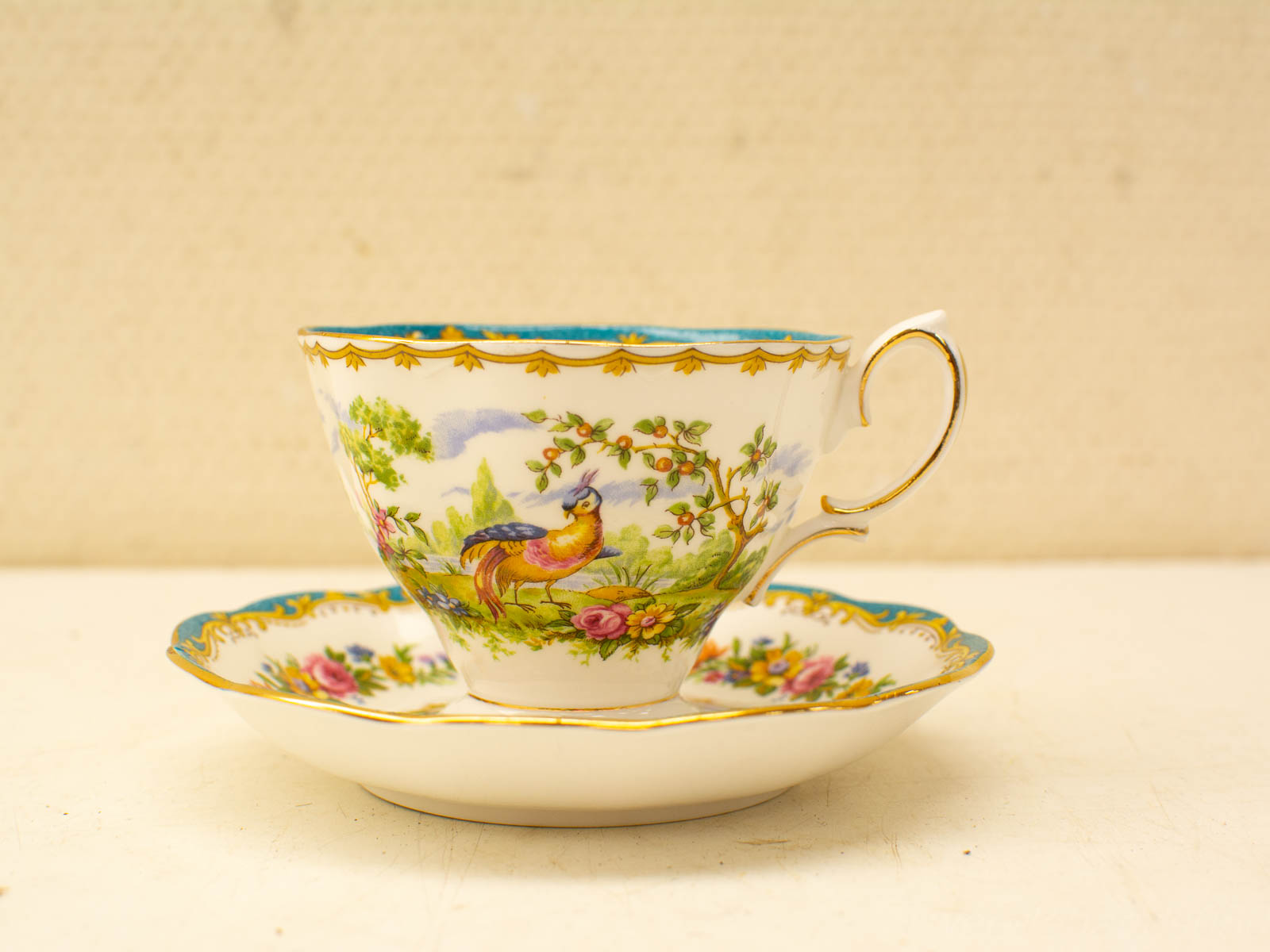 Elegant vintage porcelain teacup and saucer set with colorful bird and floral designs.